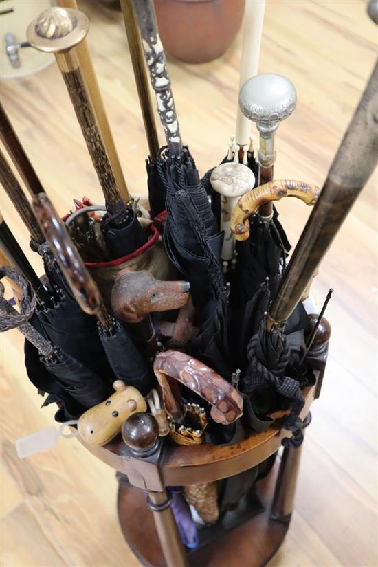 A collection of novelty and decorative parasols, contained within a cylindrical mahogany stick stand